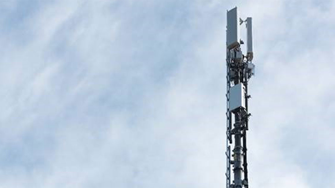 Une antenne 5G se dresse dans le ciel bleu. Des nuages blancs en arrière-plan.