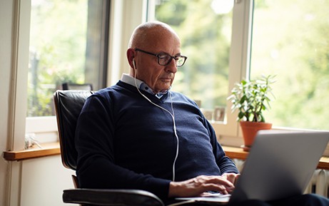 Älterer Mann surft am Laptop und trägt Kopfhörer